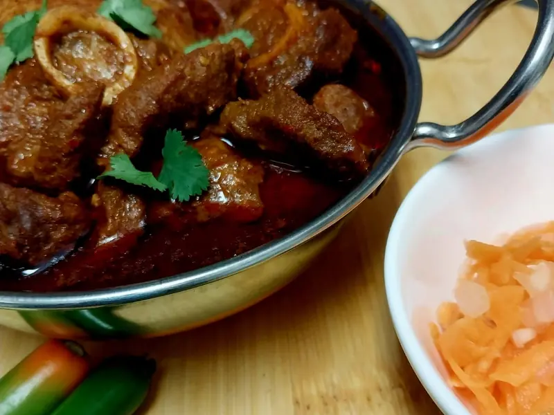 Lamb curry on the bone in a steel karahi with green chillies and carrot salad
